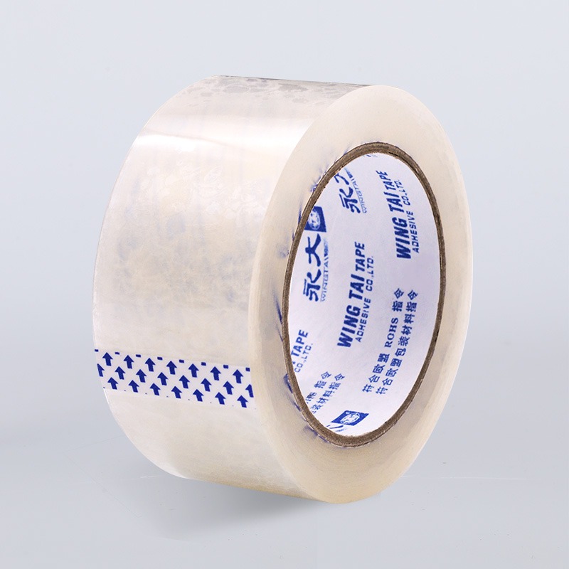 Um rolo robusto de fita acrílica bronzeada para embalagem à base de solvente com um dorso levemente texturizado e fosco; a imagem captura o calibre substancial e o vento uniforme da fita, contra uma superfície branca limpa para acentuar sua qualidade industrial.